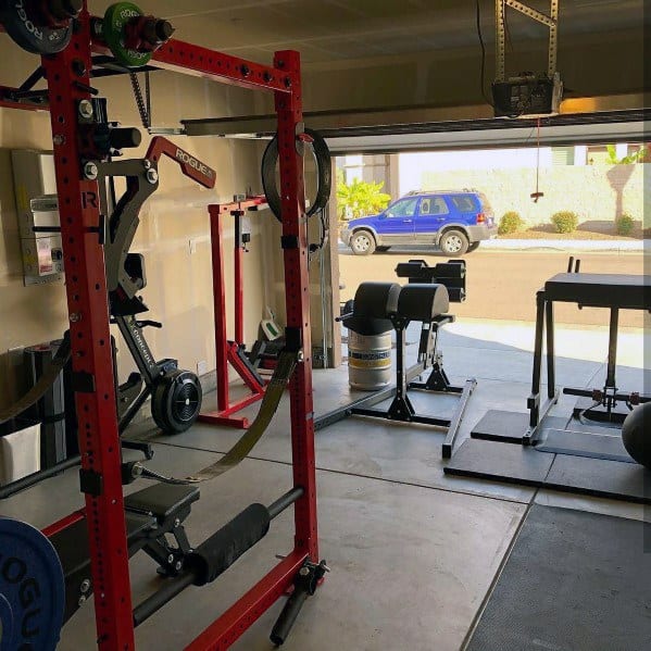 Garage gym with red power rack, GHD machine, rowing machine, and weightlifting platforms.