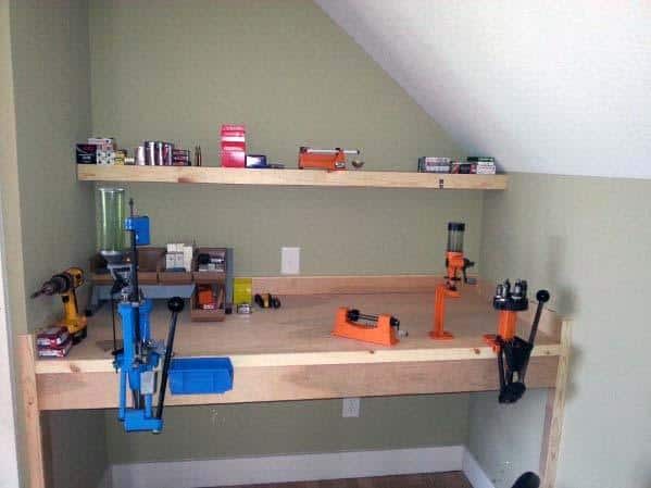 Compact reloading bench in a small corner with mounted presses, organized tools, and simple wooden shelves for supplies