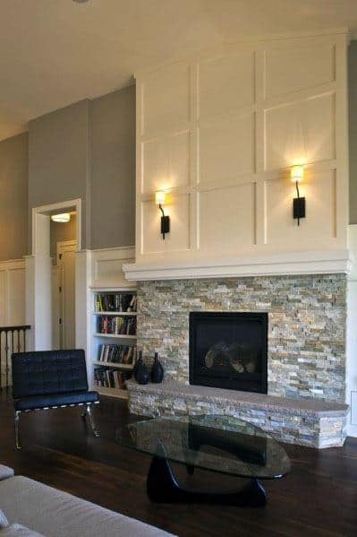 Elegant stacked stone fireplace with a white paneled wall, modern sconces, and cozy living room seating