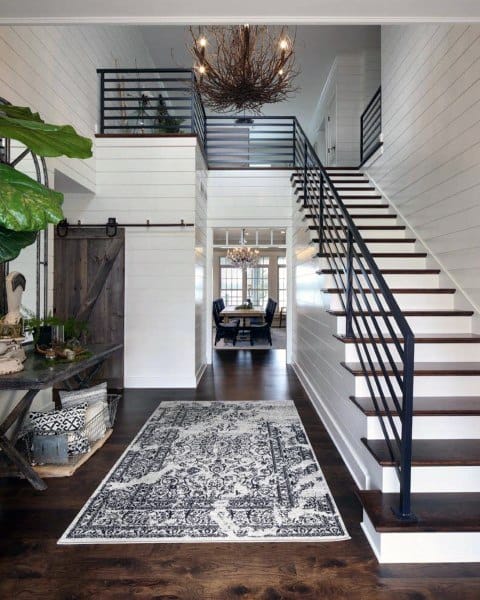 Modern entryway with dark wood floors, patterned rug, and rustic decor; a staircase leads to a visible dining area