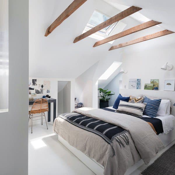 Cozy attic bedroom with skylights, wooden beams, a comfy bed, and a small corner desk with a chair