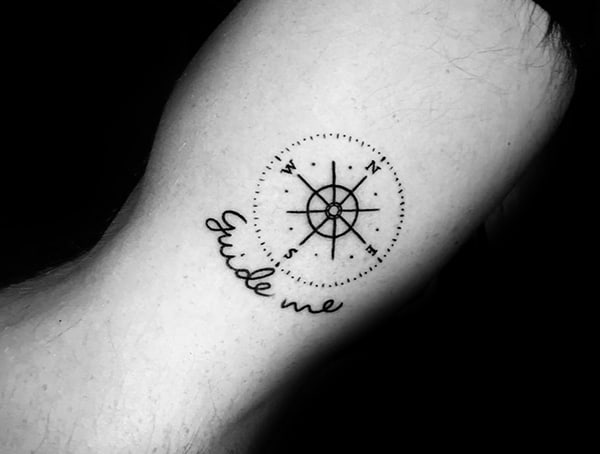 A tattoo of a compass with "Guide me" text underneath on a person's skin