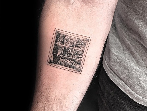 Tattoo of a square grid window on an arm, showing a detailed landscape with trees outside