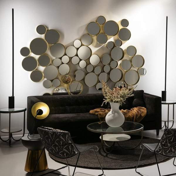 Living room with a cluster of gold-framed round mirrors, black sofa, glass tables, modern lighting, and a cozy textured throw.