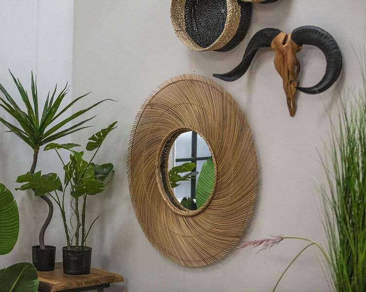 Woven rattan mirror on a neutral wall with lush green plants, woven baskets, and a sculptural ram skull for a warm, organic aesthetic.