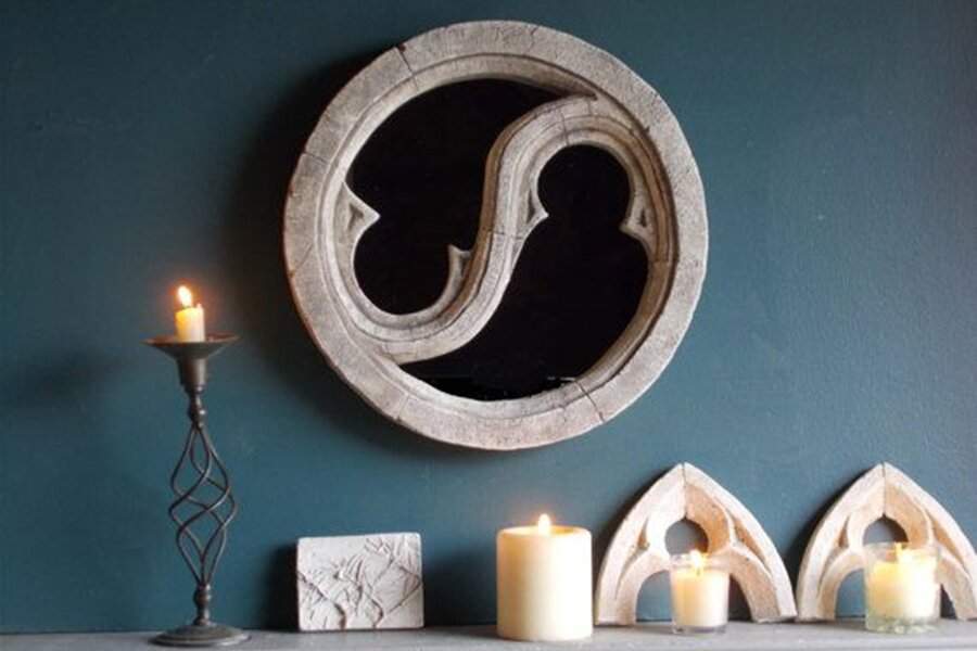 Antique-style round mirror with a sculptural frame on a dark teal wall, styled with candles and gothic-inspired decor for a moody ambiance.