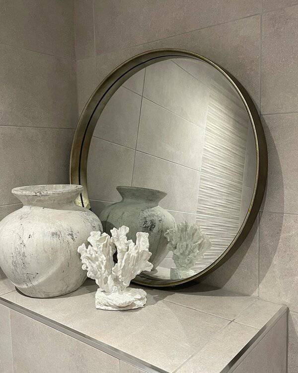 Round mirror with textured vases and white coral sculpture on a neutral-toned tiled surface for a refined, modern decor setup.