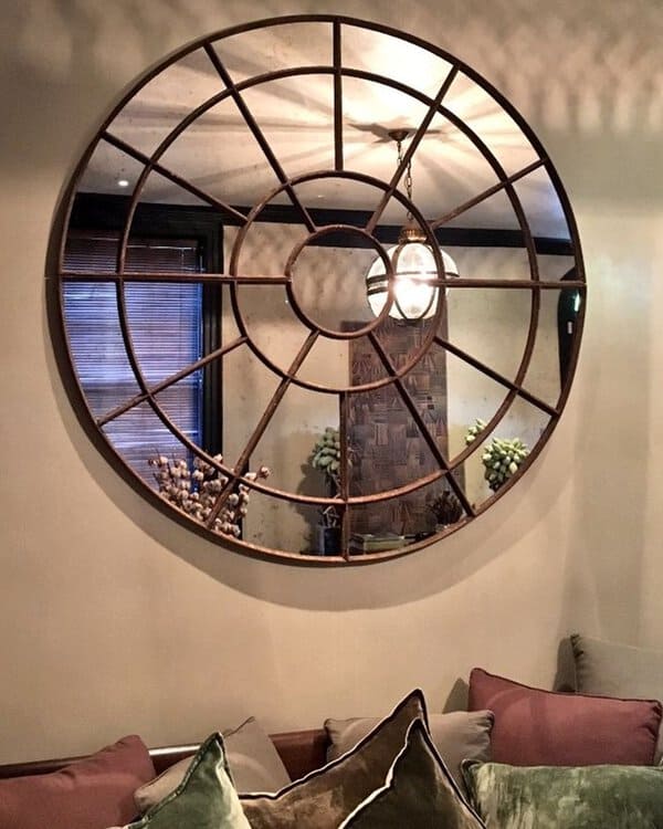 Round grid-frame mirror reflecting warm lighting in a cozy living room with plush cushions and rustic decor for an industrial-chic feel.