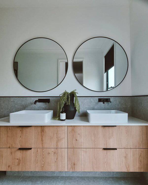 Double round mirrors above a modern bathroom vanity with wood cabinetry, black accents, and a cascading plant for a clean, balanced look.