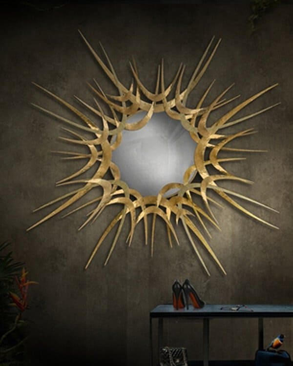 Gold sculptural sunburst mirror on a dark textured wall, creating a bold and artistic focal point in a luxurious setting.