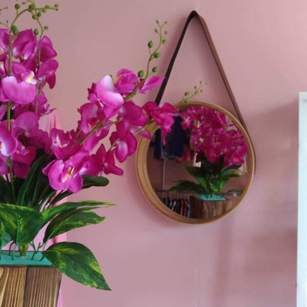 Round hanging mirror on a pink wall reflecting bright pink orchids, adding a playful and elegant touch to the space.