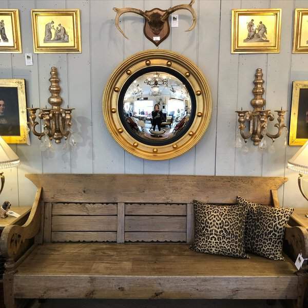 Gilded convex mirror above a rustic wooden bench, surrounded by antique sconces and artwork for a vintage yet bold statement.
