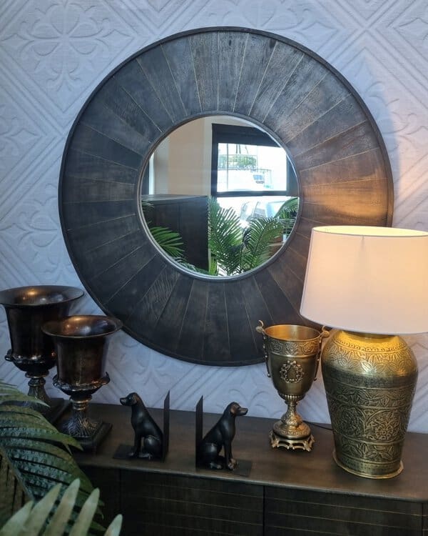 Dark-framed round mirror above a console with gold and bronze decor, blending industrial and classic elements for a sophisticated look.
