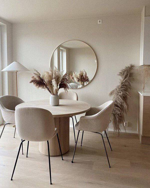 Round mirror above a wooden dining table with pampas grass, beige chairs, and soft neutral decor for a cozy, elegant dining space.