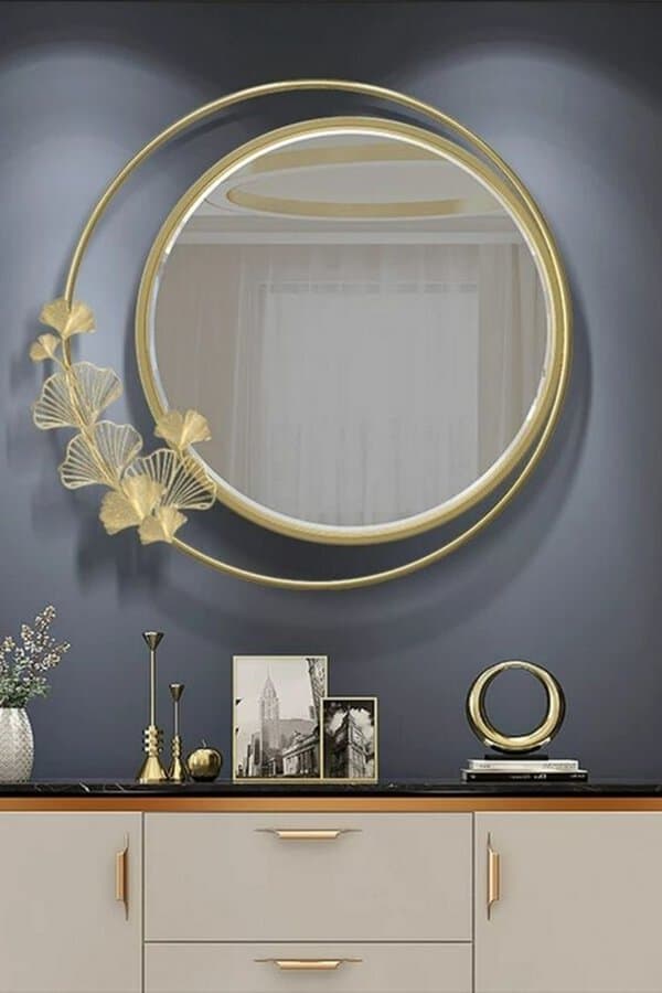 Gold-framed round mirror with floral details on a dark wall, styled with elegant metallic decor for a sophisticated, modern look.