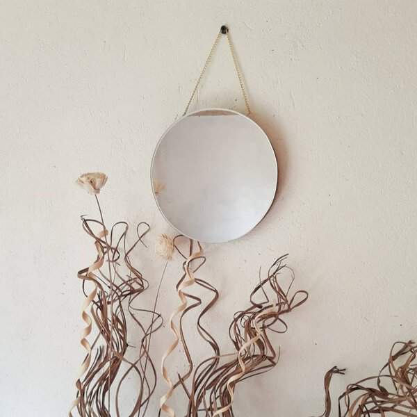 Minimalist round mirror with a delicate chain hanging on a neutral wall, framed by twisting dried branches for an organic, artistic look.