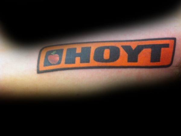 Bold forearm tattoo of the HOYT archery logo in black and orange, featuring a red apple symbol inside the letter O.