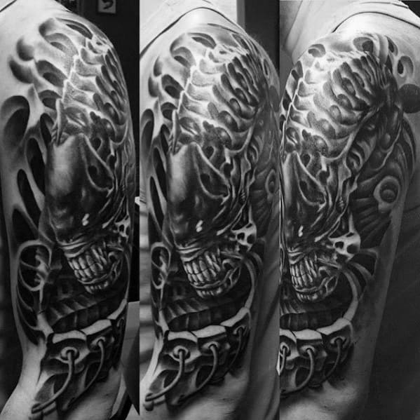 HR Giger-style upper arm tattoo featuring a menacing xenomorph head with biomechanical textures and intense black and grey shading.