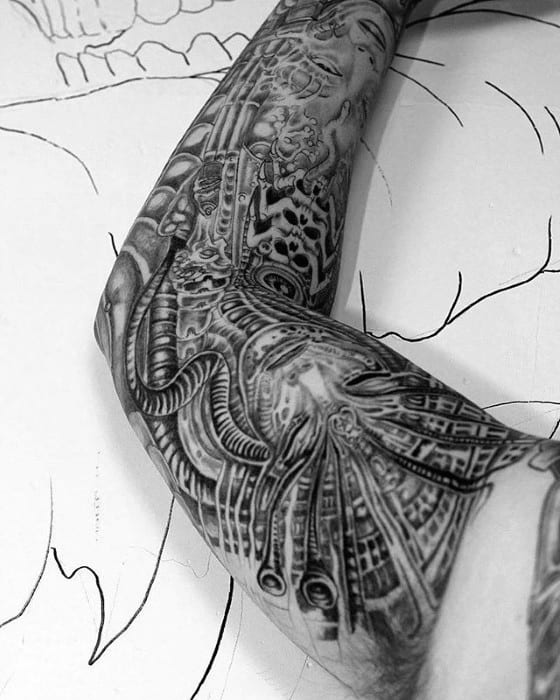 HR Giger-inspired arm tattoo with intricate biomechanical patterns, alien tubing, and surreal facial elements blended into machinery.