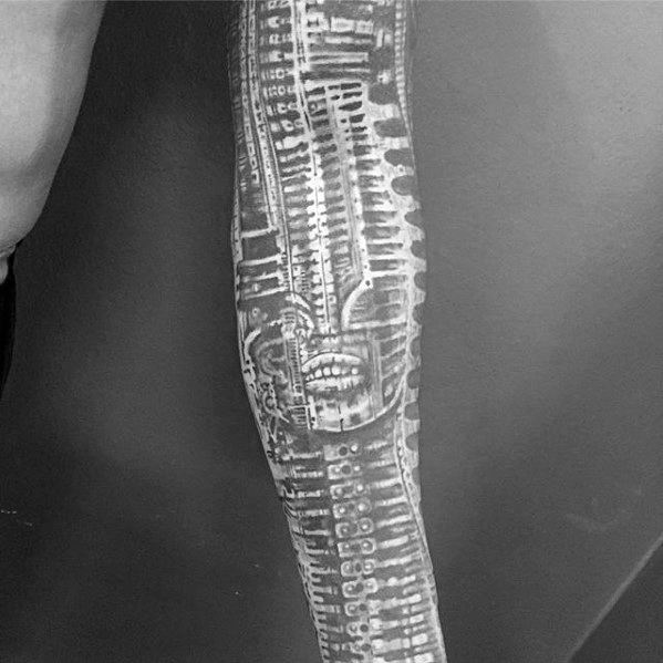 HR Giger-style forearm tattoo featuring an abstract biomechanical face fused with circuit-like patterns and alien skeletal textures.