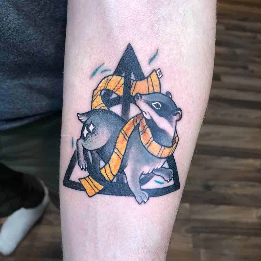 Colorful Deathly Hallows tattoo featuring a Hufflepuff badger wrapped in a yellow and black scarf, with a bold, stylized design.