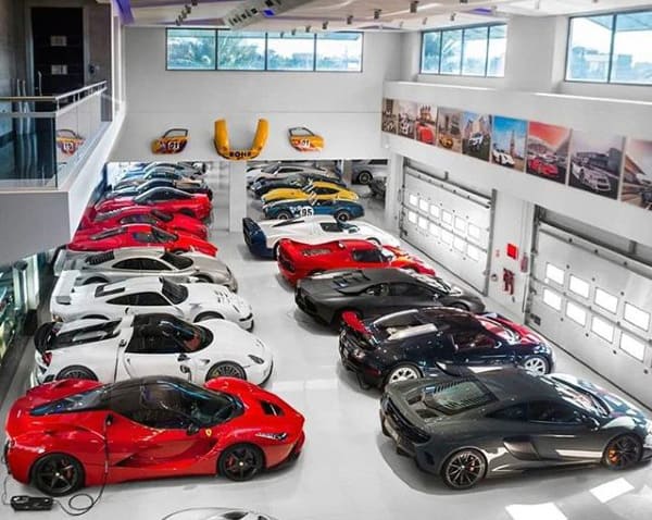 A spacious, high-end garage showcasing a vast collection of exotic supercars, pristine white floors, and modern decor.