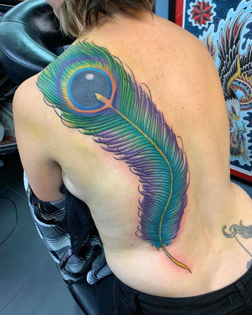 Large, vibrant peacock feather tattoo covering the back, featuring rich blue, green, and purple hues with intricate shading and fine details.