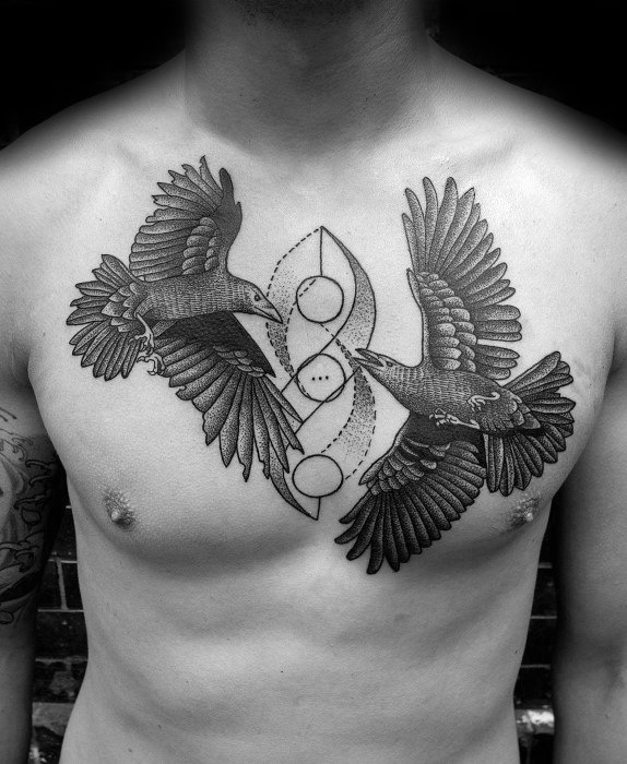 Symmetrical chest tattoo of Huginn and Muninn in flight with detailed wings, circling a Norse-inspired symbol at the center.