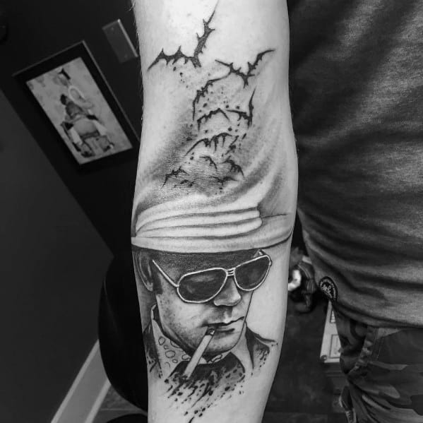 Black and white Hunter S. Thompson tattoo featuring a detailed portrait with aviator glasses, a cigarette, and bats flying from his hat in a surreal style.