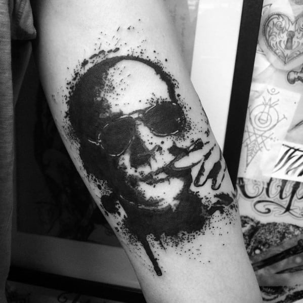 Black and white Hunter S. Thompson tattoo featuring a splatter ink effect, with aviator glasses, a cigarette, and a raw, artistic portrait style.