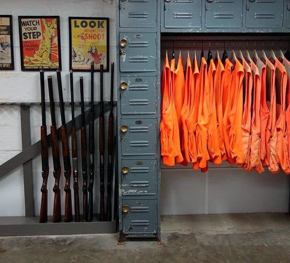 Functional hunting room with vintage lockers, gun racks, and bright orange vests neatly organized for quick access.