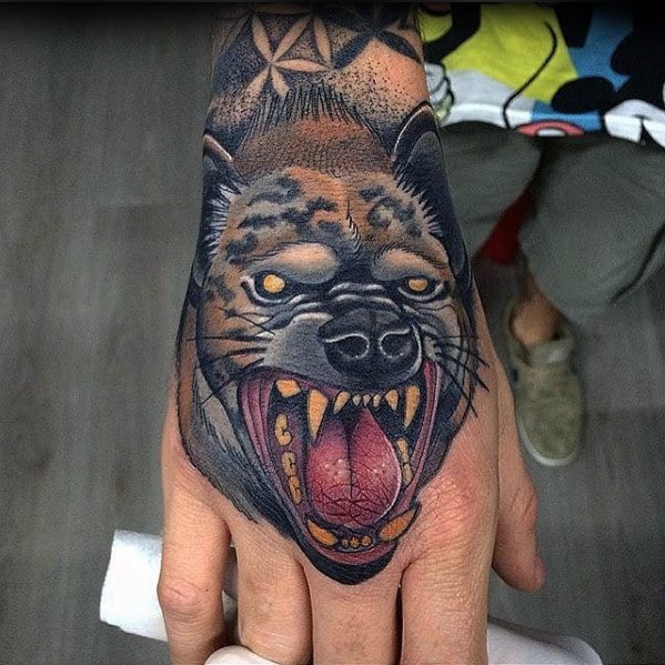 Realistic hyena tattoo on the hand with sharp fangs, piercing yellow eyes, and a wide open mouth, blending vivid color with bold detail.