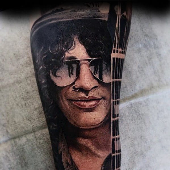 Realistic tattoo of Slash with curly hair, sunglasses, a nose ring, and a guitar neck beside his face, capturing his iconic rock style.