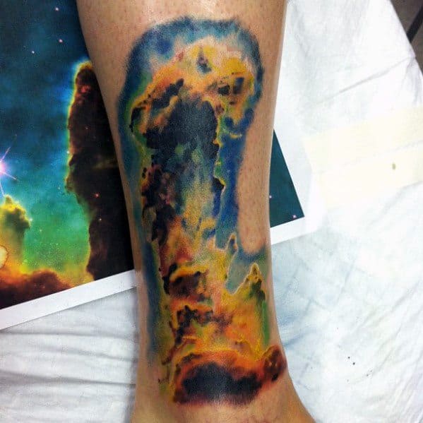Colorful nebula tattoo on a leg, showcasing a cosmic scene with vibrant blues, oranges, and yellows