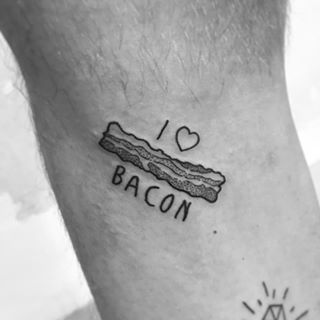 A simple black ink tattoo of a strip of bacon with the phrase 'I ♥ BACON,' designed in a minimalist and playful style.