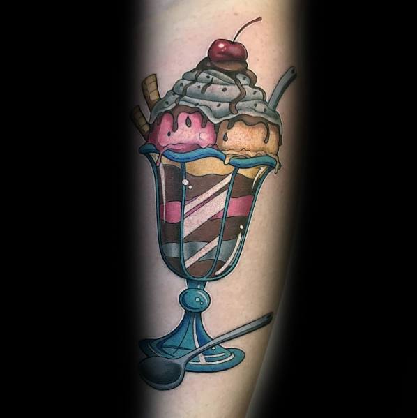 Tattoo of a colorful ice cream sundae in a glass cup with whipped cream, wafers, a cherry on top, and a spoon resting beside it.