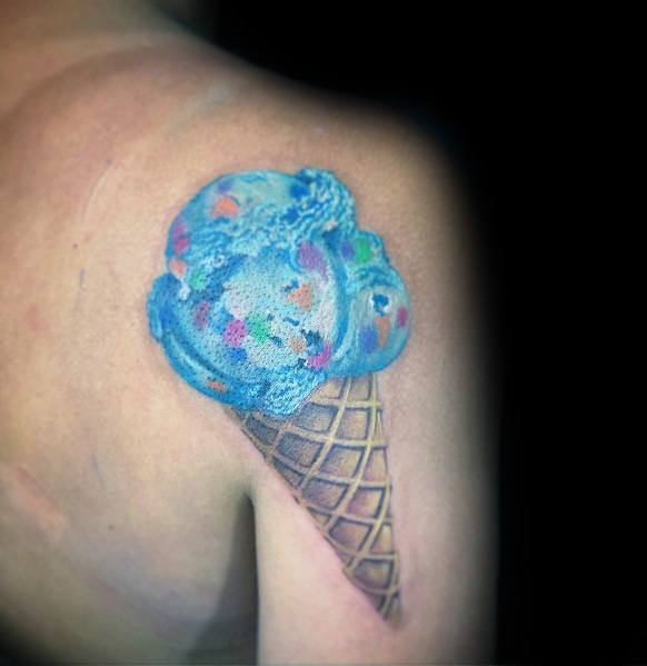Realistic tattoo of a blue ice cream scoop with colorful sprinkles in a detailed waffle cone, creating a vibrant and textured 3D effect.