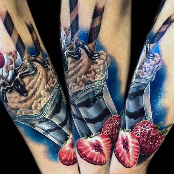 Hyper-realistic tattoo of a chocolate milkshake in a glass with dripping syrup, striped straws, and fresh strawberries, featuring vibrant colors and shading.