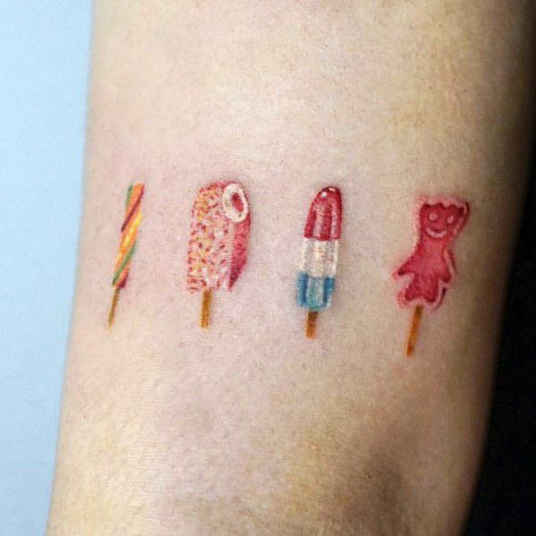 Minimalist tattoo of four small, colorful popsicles in different shapes and textures, including a gummy bear design, creating a playful and nostalgic look.