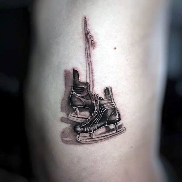 Realistic black and grey tattoo of a pair of hanging ice skates tied together by their laces, symbolizing a passion for skating or hockey.