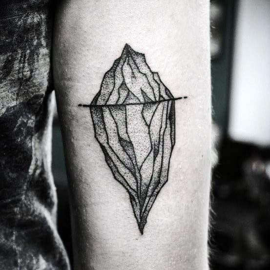 Dotwork iceberg tattoo with bold outlines and detailed shading, featuring a horizontal waterline across the design on the forearm.