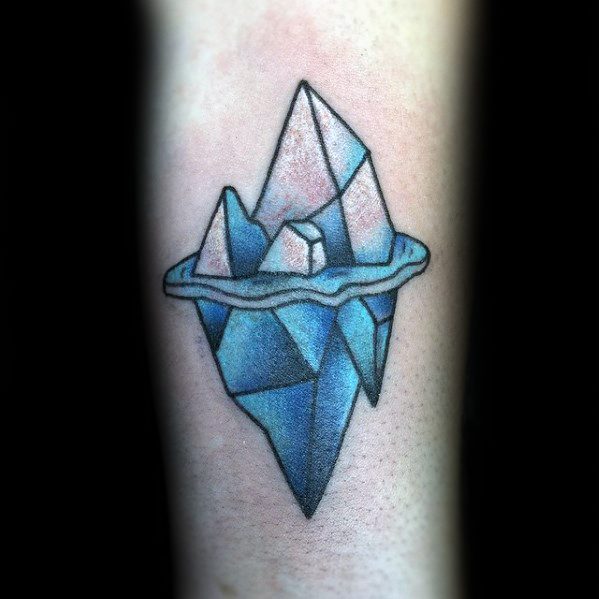 Bold blue iceberg tattoo with sharp geometric facets and soft pink highlights, floating in icy water on the forearm.