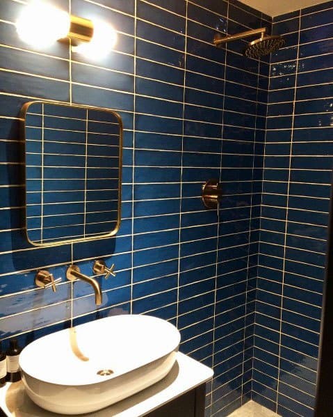 Bathroom with deep blue tiles, gold fixtures, round vessel sink, and illuminated mirror.
