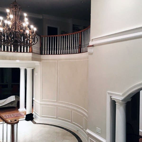 Elegant interior with a grand staircase, chandelier, chair rail, and white columns in a luxurious setting