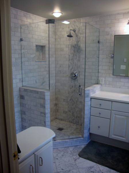 Modern bathroom with a corner glass-enclosed shower, white tiles, and a vanity with drawers