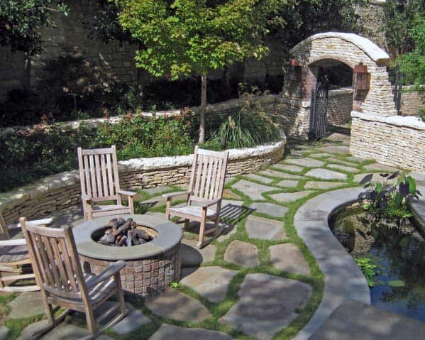 Garden with stone path, wooden chairs around a fire pit, a pond, and an arched stone gate