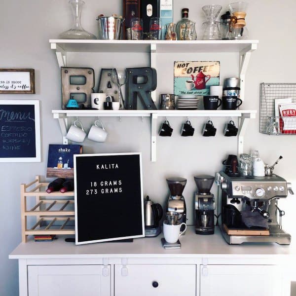 Eclectic coffee bar with white shelves, espresso machine, mugs, decor, and letter board.