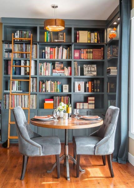 Cozy dining area with a round table, two gray chairs, and a bookshelf filled with books and records in the background