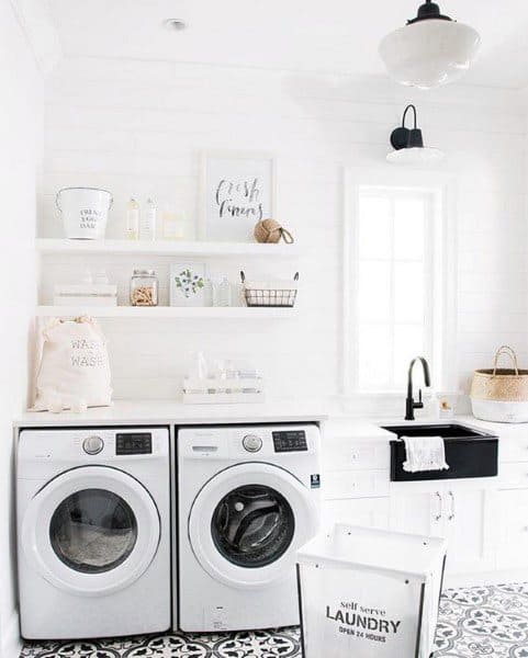 Bright laundry room with white appliances, open shelves, black sink, and patterned tile flooring.