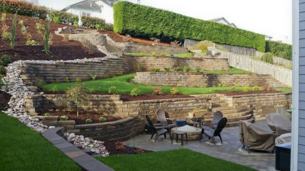 Tiered retaining walls with landscaping, a patio area, and outdoor seating with a fire pit.